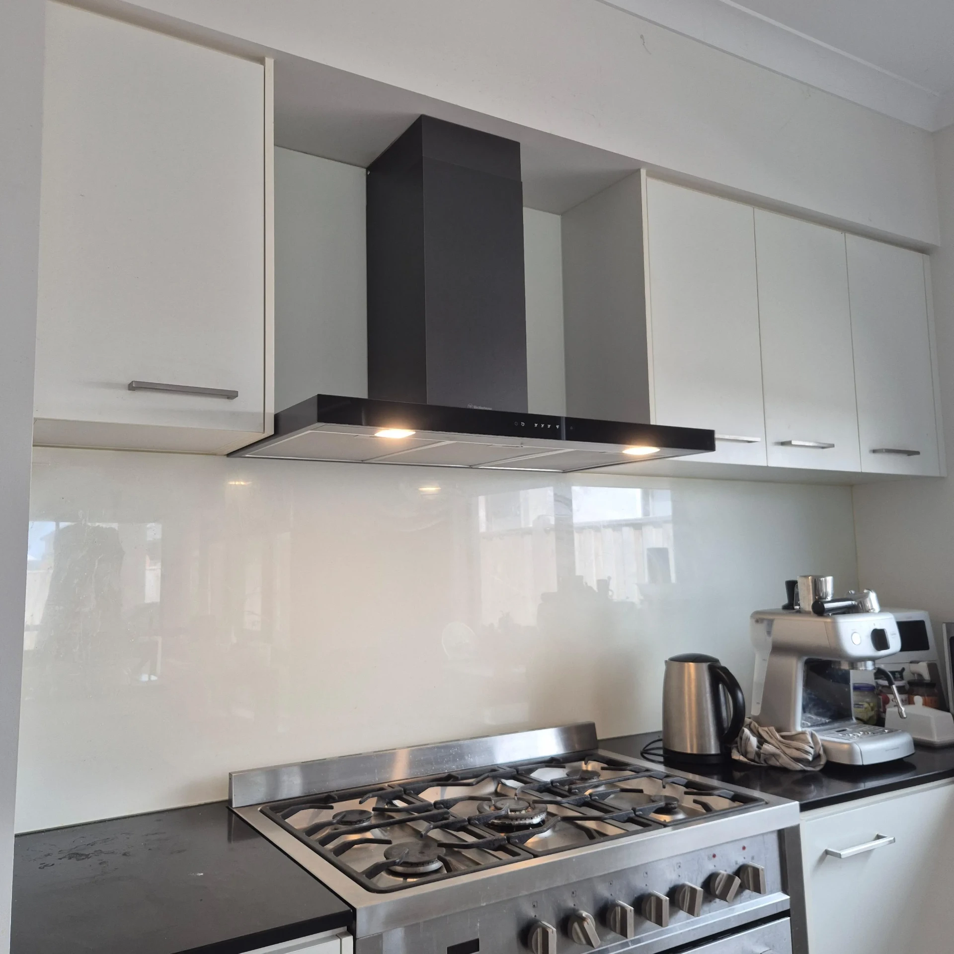 Black canopy rangehood installed above a gas cooktop